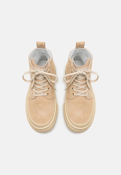 Beige suede high-top sneakers with cream laces, rounded toe, thick soles, and rear pull tabs. Interior lined in white material.