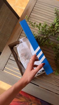 Blå boks med hvit sikksakk-design, som inneholder papirservietter og sko, hviler på en tresoverflate med en plante i bakgrunnen.