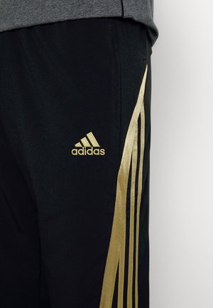 Schwarze Adidas-Sporthose mit goldfarbenem Logo und goldfarbenen Streifen an der Seite, kombiniert mit einem grauen Oberteil.