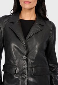 Černý kožený kabát s klopovým límcem, zapínáním na dva knoflíky a dvěma předními kapsami. Hladká textura a přiléhavý střih.
