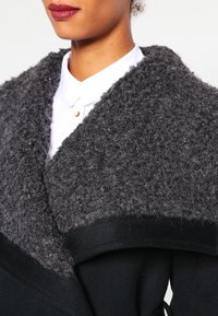 Cappotto nero con colletto testurizzato grigio e peloso. Presenta un ampio risvolto e una silhouette liscia e strutturata.