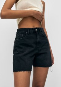 Zwarte denim shorts met een uitgerafelde zoom, klassiek vijf zakken ontwerp en knoopsluiting. De stof lijkt stevig met een gladde textuur.