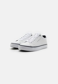 Baskets blanches avec une tige en cuir lisse, bout rond et semelle bleu marine contrastante. Comprend six œillets, des lacets plats et un détail logo.