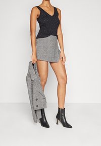 Haut sans manches noir avec des rivets métalliques, associé à une mini jupe en pied-de-poule. Bottines noires à bout pointu avec des accents dorés.