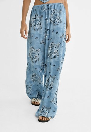 Luźne, jasnoniebieskie spodnie z białymi i czarnymi wzorami paisley, z wiązanym w pasie ściągaczem, noszone z białymi sandałami, odsłaniającymi palce u stóp.