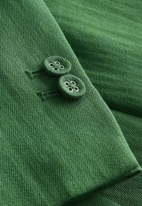 Tissu tricoté vert avec deux boutons verts assortis cousus très près l’un de l’autre près d’un bord plié.