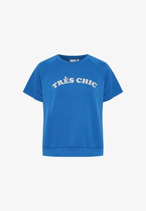 Blå bomullströja med korta raglanärmar. Har frasen "TRÈS CHIC" i stora vita bokstäver över framsidan.