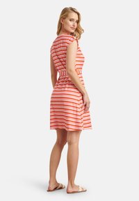 Rood-wit gestreepte jurk met een getailleerde taille, korte mouwen en een uitlopende rok. Gemaakt van een gestructureerde stof; gecombineerd met lichte sandalen.