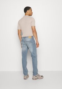 Polo de manga corta en beige claro con un patrón de punto texturizado, combinado con jeans de mezclilla azul claro. Etiqueta marrón notable en la parte trasera de los jeans.