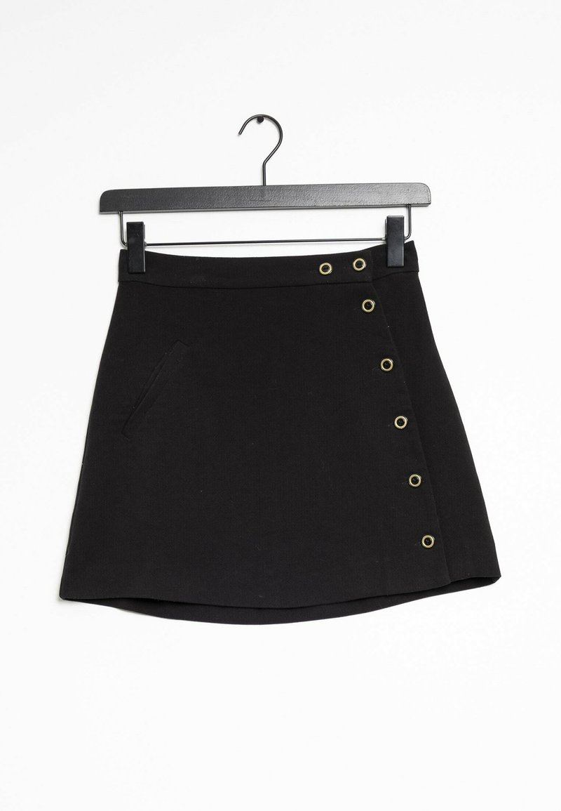 Mini-jupe noire avec poche latérale et six œillets métalliques, suspendue sur un cintre noir sur fond blanc.