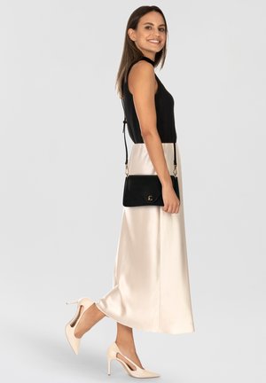 Schwarzes, geripptes ärmelloses Oberteil, cremefarbener Satin-Midirock, schwarze Umhängetasche, beige High-Heels mit Cut-out-Design.