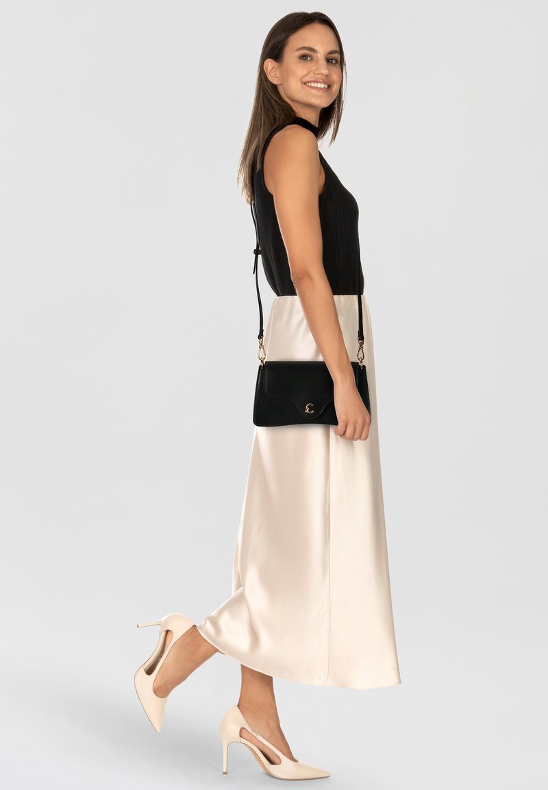 Top nero senza maniche a coste, gonna midi color crema in raso, borsa a tracolla nera, scarpe con tacco alte color beige con design traforato.