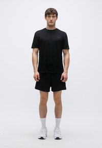 Svart atletisk t-shirt och shorts i lättviktstyg, med rund halsringning och korta ärmar. Bärs med vita sneakers och strumpor.