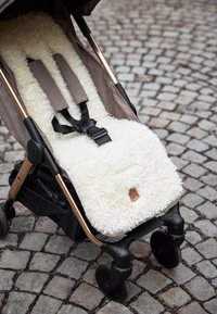 Empty baby stroller with black harness and white fluffy seat liner on cobblestone pavement.
