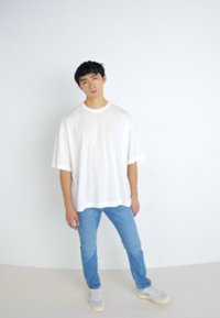 Camiseta blanca de gran tamaño con mangas cortas, combinada con jeans de color azul claro y zapatillas grises. Fondo neutral, diseño minimalista.