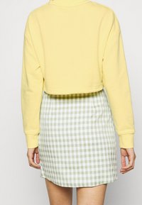 Sweat-shirt jaune court à manches longues, associé à une mini-jupe à motifs vichy verts et blancs. Le matériau semble doux et décontracté.