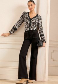 Blusa nera con stampa floreale, maniche a sbuffo e scollatura a V, abbinata a jeans neri a vita alta e tacchi beige con punta. Borsa clutch nera.