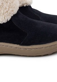 Calzature in suede blu scuro con fodera in finta pelliccia crema al polsino. Presentano una suola in gomma color nocciola con dettagli testurizzati e accenti di cucitura.