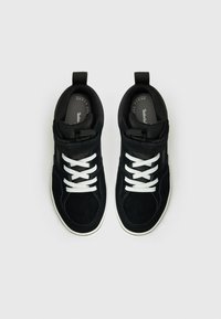Sorte semskede sneakers med hvite lisser og gummisåler. Har polstret krage og tunge, teksturert stoff og minimalistisk design.