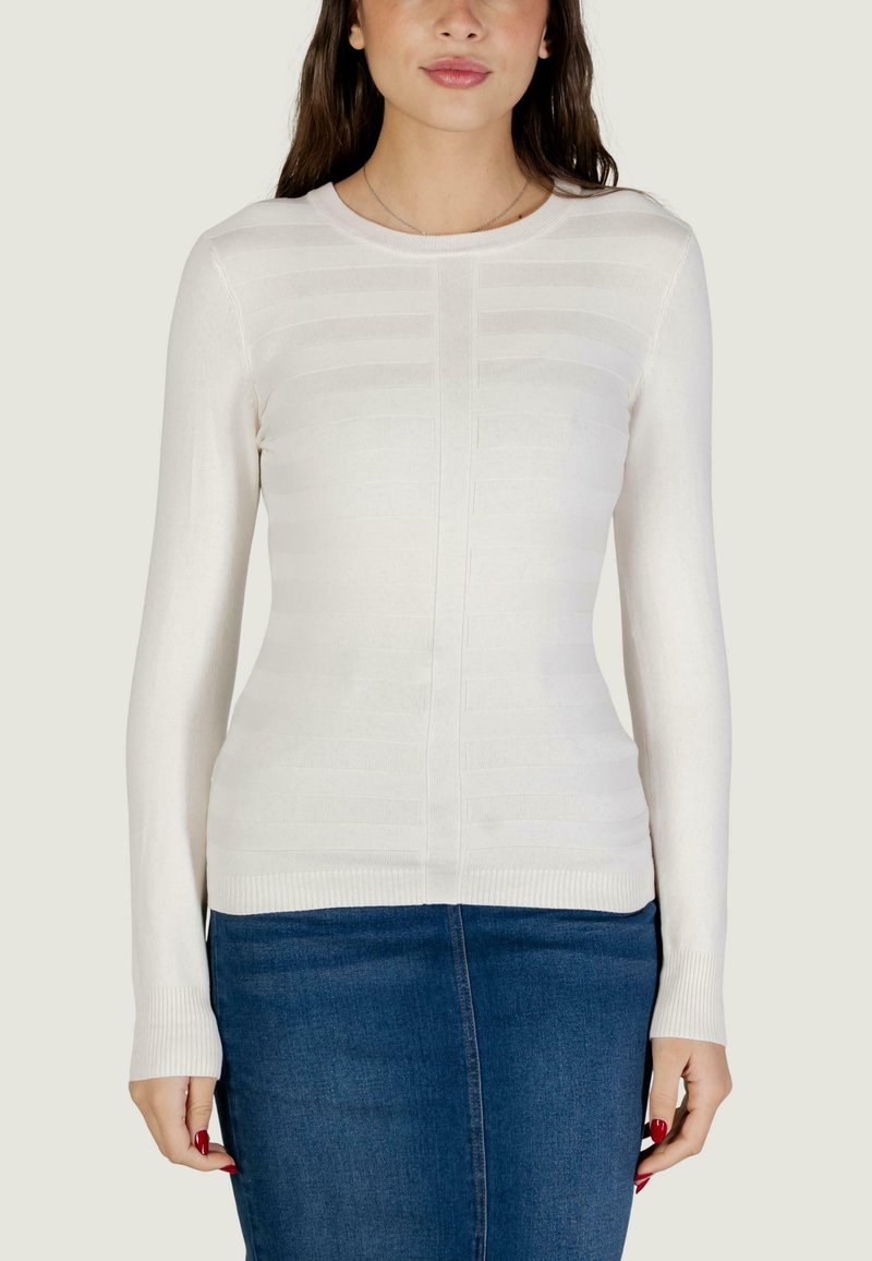 Pull crème en tricot à manches longues, avec des motifs à rayures horizontales et un ourlet côtelé. Associé à une jupe en denim.