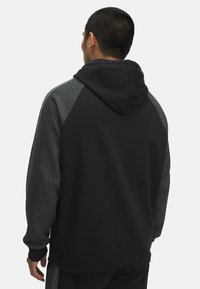 Schwarzer Kapuzenpullover mit grauen Akzenten an den Ärmeln und der Kapuze. Er weist eine weiche Textur, eine Kängurutasche sowie gerippte Bündchen und Saum auf.