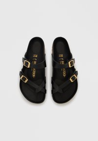 Μαύρα σανδάλια με πάτο από φελλό, με δύο ρυθμιζόμενους ιμάντες με χρυσά αγκράφες. Λείο επιφάνεια και εργονομικός σχεδιασμός για άνεση.