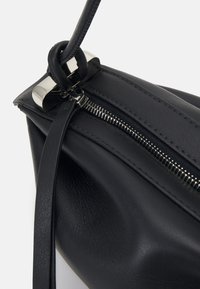 Black leather handbag with a smooth texture, silver zipper, and a looped handle design. Features a structured shape and minimalistic accents.