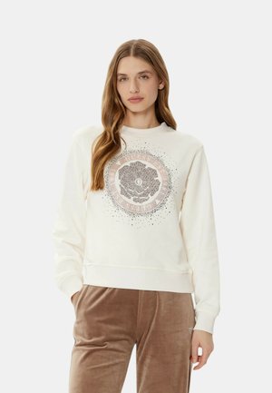 Felpa cremosa con una grafica rotonda floreale in rosa e nero. Tessuto morbido, polsini e vita a coste. Abbinata a pantaloni in velluto marrone.