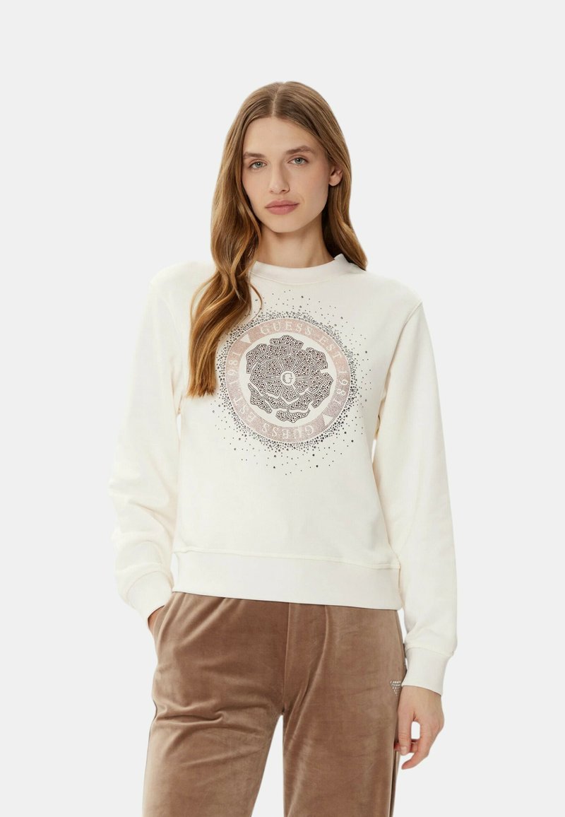 Felpa cremosa con una grafica rotonda floreale in rosa e nero. Tessuto morbido, polsini e vita a coste. Abbinata a pantaloni in velluto marrone.
