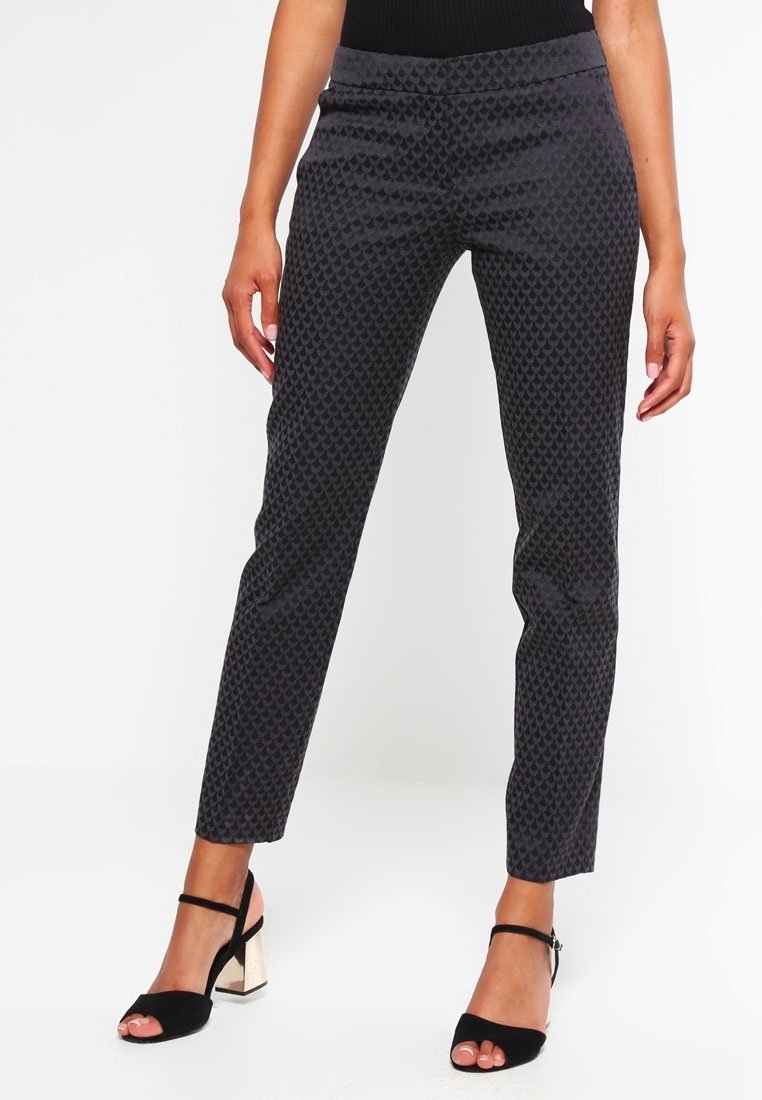 Pantalon noir à motif avec une coupe ajustée, une texture lisse et une ceinture taille mi-haute. Porté avec des talons noirs à lanières dotés d'un talon bloc.