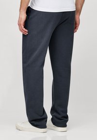 Navy sweatpants with a straight-leg design, elastic waistband, side pockets, and soft texture, paired with white sneakers.