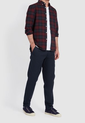 Camisa de cuadros roja y negra, llevada sobre una camiseta blanca. Pantalones azul marino oscuro y zapatillas azul marino con suelas crema complementan el conjunto.