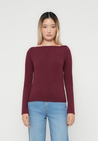 Bordeaux lange mouwen top met een brede bootnek, gemaakt van een zachte stof. Draagt met lichtblauwe high-waisted jeans. Eenvoudig en aansluitend ontwerp.