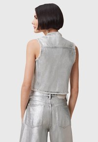 Gilet in denim argento con bordi sfrangiati, abbinato a pantaloni a vita alta metallici argento con tasche posteriori e una finitura elegante.