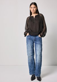 Schwarze transparente Bluse mit Rundhalsausschnitt und Frontreißverschluss, kombiniert mit hellblauen geraden Jeans und schwarzen Ankle-Boots.