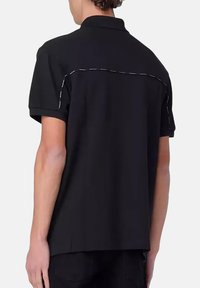 Polo noir à manches courtes, avec un col classique et des coutures blanches contrastées au dos, fabriqué en un mélange de coton lisse.