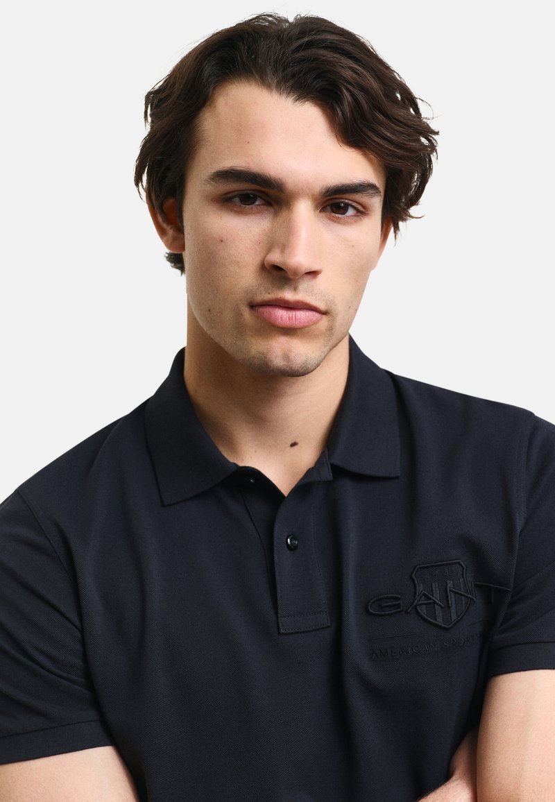 Navy Poloshirt aus strukturiertem Stoff, mit einem klassischen Kragen und gesticktem Logo auf der linken Brust. Kurzarm, klassische Passform.