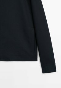 Zwarte jacksleeve met een rechte snit, voorzien van een stijlvolle textuur en een onzichtbare zijzak. Eenvoudig ontwerp zonder zichtbare hardware.