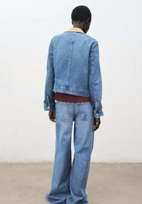 Denim jacket with a light blue wash and beige collar, paired with wide-leg light blue jeans. Features a classic cut and visible stitching.
