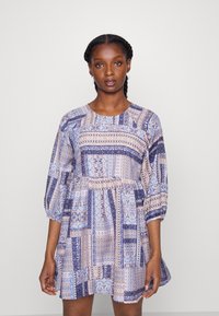 Vestido de manga curta em padrão de patchwork com cores azuis, lavanda e creme. Apresenta um decote redondo e cintura franzida para uma saia rodada.