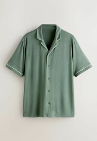 Chemise boutonnée à manches courtes vert sauge avec un liseré blanc le long du col, de l'avant et des bords des manches, présentée sur un fond neutre.