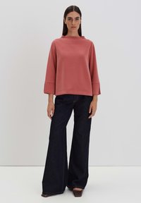 Rust-colored top with wide sleeves, paired with high-waisted dark denim flared pants, creating a relaxed silhouette.