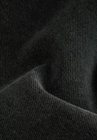 Tejido negro de punto con una superficie suave y texturizada, que muestra un fino canalé y pliegues suaves, resaltando su profundidad y rico color.