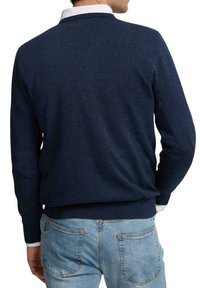 Jersey de punto azul marino con cuello redondo, puños y dobladillo acanalados. Llevado sobre una camisa blanca con cuello, mostrado desde la parte posterior.