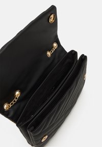 Borsa a tracolla in pelle nera con un design trapuntato, dotata di una chiusura a scatto dorata e dettagli in catena. L'interno include più scomparti.