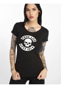 Juodas medvilnės T-shirt su baltu grafikos dizainu, kuriame pavaizduotas kaukolė ir tekstas „THUG LIFE EST. 187.“ Trumpomis rankovėmis ir apvaliu iškirpimu.