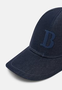 Casquette de baseball en denim bleu foncé avec la lettre "B" brodée sur le panneau avant et des coutures apparentes sur la visière et les coutures.