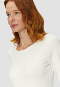 Weißes Langarmoberteil mit rundem Ausschnitt. Glatte Textur, taillierte Form und minimalistisches Design ohne sichtbare Muster oder Akzente.