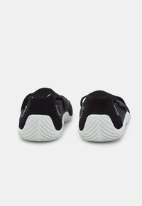 Zapatillas deportivas negras con parte superior de tejido texturizado, correas elásticas y una suela de goma blanca con un patrón en zigzag.