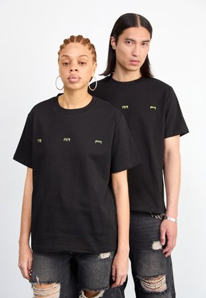 Schwarze Baumwoll-T-Shirts mit minimalen grünen Textdetails auf der Brust, kombiniert mit ausgewaschenen schwarzen Jeans. Einfaches, geradliniges Design.